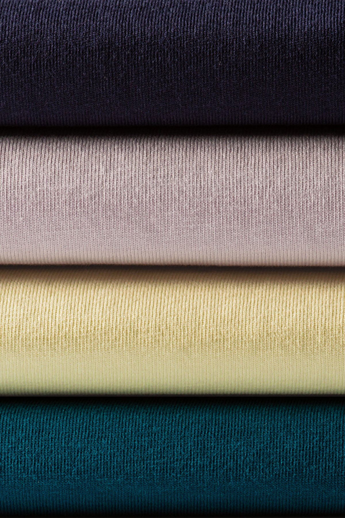 Stack of four neatly folded classic heavyweight ribbed knit t-shirts in navy mauve pale yellow and teal for workwear uniforms
