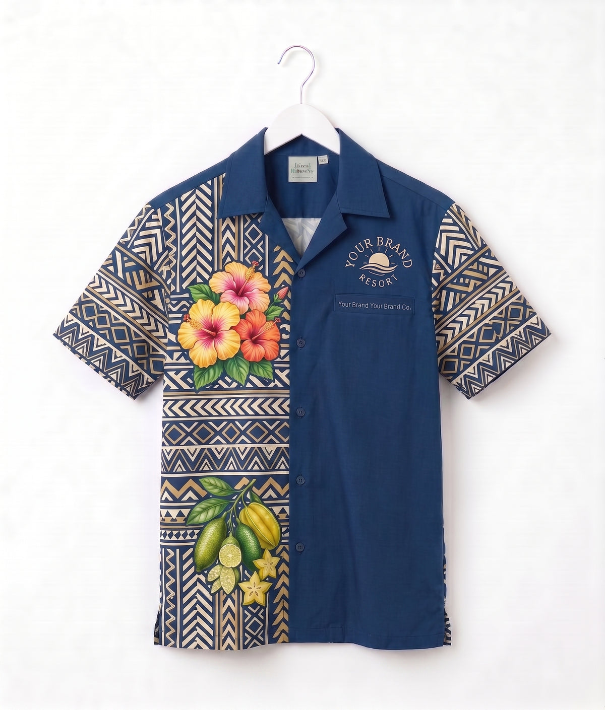 A short-sleeve button-up camp shirt hanging on a white hanger against a white wall. The shirt features a navy blue body with geometric patterned sleeves and lower front panel, decorated with tropical floral and fruit prints including hibiscus flowers and bananas.