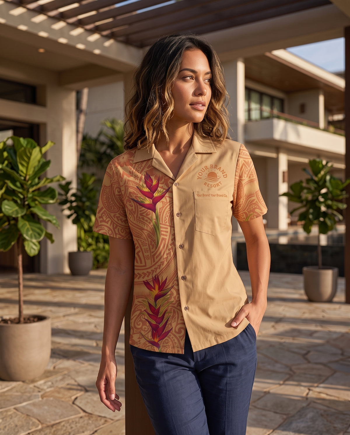 A woman stands outdoors in a tropical resort setting wearing a beige short-sleeve camp collar shirt with brown tribal-style patterns and red tropical floral prints, paired with navy pants.