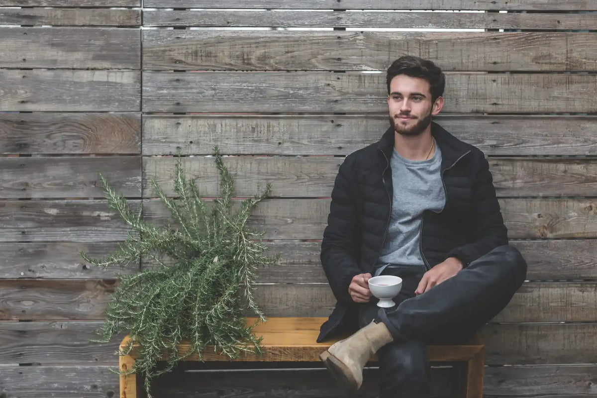 Man in puffer jacket and work pants drinking a coffee