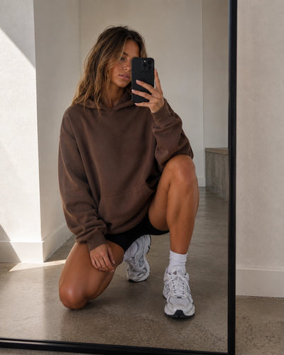 Person wearing a brown 'planett.' hoodie taking a mirror selfie.