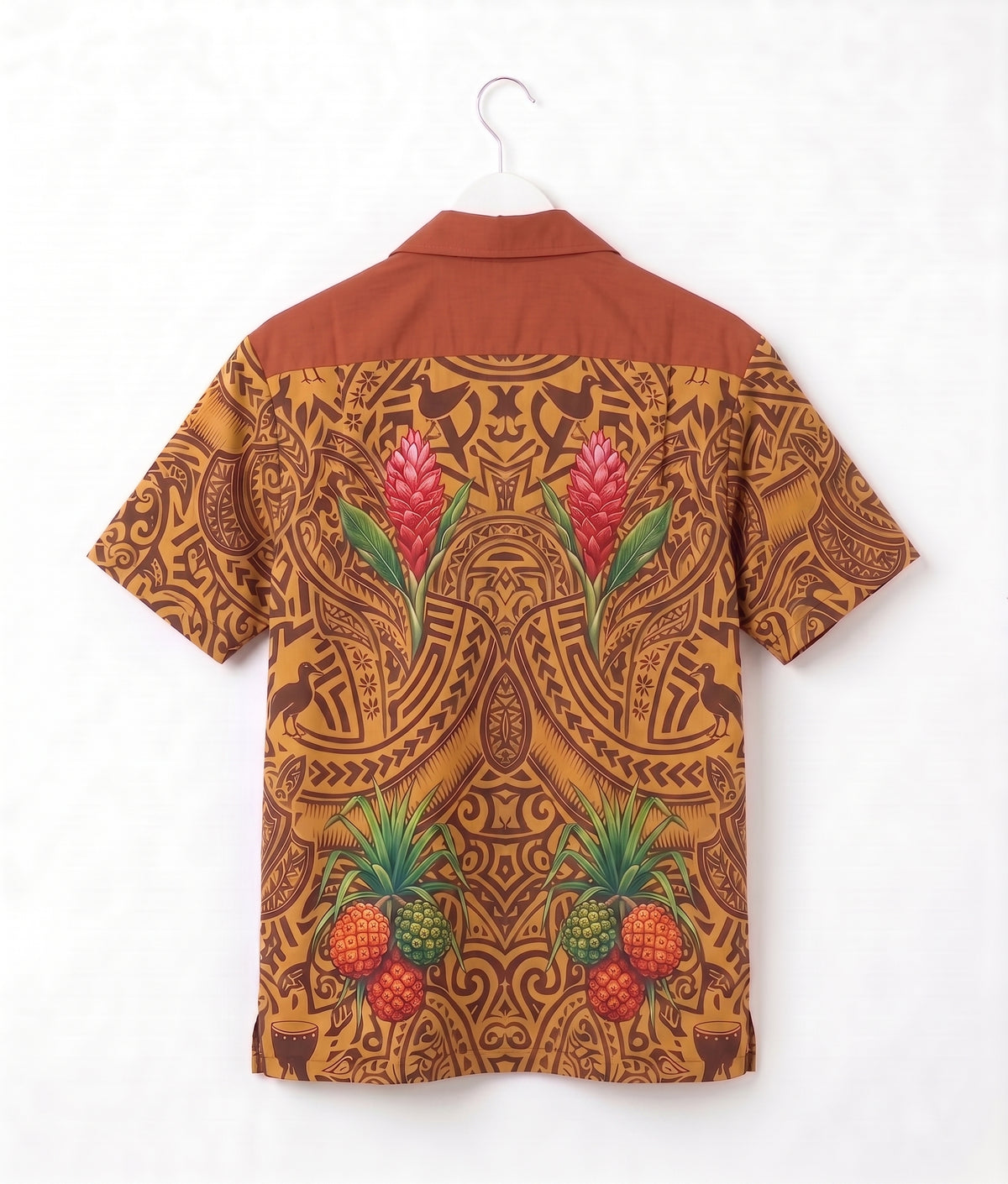 A short-sleeve camp collar shirt shown from the back, hanging on a white hanger against a white wall. The shirt features a warm rust-brown yoke and a back print in a golden-brown tribal pattern decorated with pink tropical flowers and green pineapples.